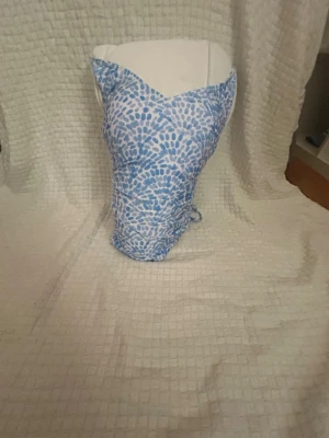 Blåvit baddräkt med snörning - Snygg baddräkt i blått och vitt mönster med trendig snörning i ryggen. Baddräkten har en hjärtformad urringning och smala axelband som korsas i ryggen. Tillverkad i stretchigt material som passar perfekt för stranden eller poolen.