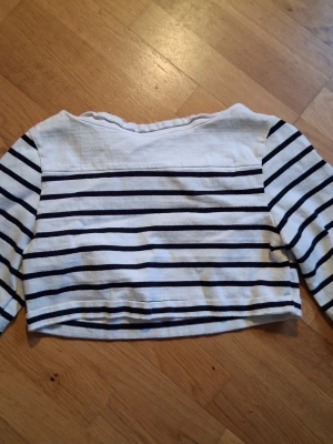 Vit och marinblå randig croptröja - Säljer en croppad långärmad tröja med marinblå och vita horisontella ränder. Tröjan har en avslappnad passform och är tillverkad i ett mjukt bomullsliknande material. Perfekt för en casual look.