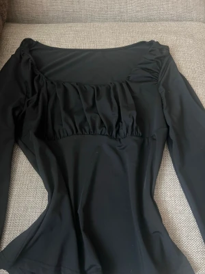 Svart långärmad topp med rynk - Svart långärmad topp med rynkdetalj över bysten och fyrkantig ringning. Sitter figurnära och har en stilren, enkel look som passar till många outfits. Tillverkad i ett stretchigt syntetmaterial för en bekväm passform.Pris går o diskutera , använd fåtal tillfällen💞 