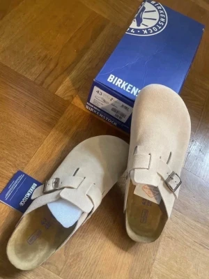 Birkenstock Boston beige mocka tofflor - Snygga beige Birkenstock Boston tofflor i mocka med klassisk design och justerbart spänne i metall. Mjukt innersula för extra komfort.                Skickar inom 24h✅.