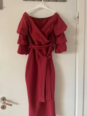 Röd klänning  - Snygg röd från Boohoo med volangärmar och knytband i midjan. Klänningen har v-ringning och är tillverkad i ett lätt, strukturerat tyg. 