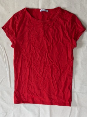 Röd t-shirt från Zara - En enkel och stilren röd t-shirt från Zara med rund halsringning och korta ärmar. Tillverkad i mjuk bomull som känns skön mot huden. Använd ett fåtal gånger.