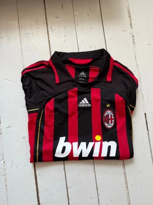 AC Milan matchtröja Kaka #22 Adidas - Säljer en klassisk AC Milan matchtröja från Adidas med Kaka och nummer 22 på ryggen. Tröjan är svart och röd med gula detaljer, klubbmärke och Bwin-logga på bröstet. Perfekt för dig som älskar fotboll och vill ha en ikonisk supportertröja.