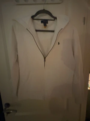 Vit hoodie från Polo Ralph Lauren. Storlek XL, men för barn! Passar xs-s vuxen  - Snygg vit hoodie från Polo Ralph Lauren med dragkedja framtill och klassisk huva. Ikoniska Polo-loggan broderad på bröstet. Tillverkad i mjukt material som känns skönt mot huden. Perfekt för en clean och stilren look. Passar xs-s vuxen!XL-barn. Passar mig bra, är 178. ALDRIG använd. Köpte fel o säljer därför 