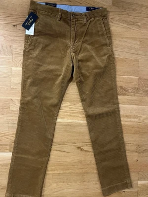 Bruna manchesterbyxor från Polo Ralph Lauren - Snygga bruna manchesterbyxor från Polo Ralph Lauren med klassisk rak passform och diskreta fickor. Byxorna har bälteshällor och stängs med dragkedja och knapp. Perfekta för dig som gillar en tidlös och stilren look. W31 L32