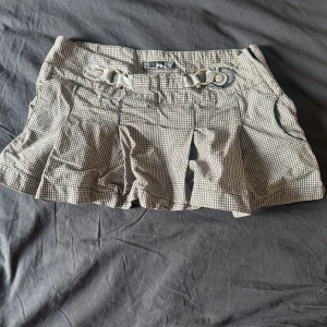 Rutiga skorts från Tally Weijl - Snygga rutiga skorts från Tally Weijl i svart och vitt. Modellen har dekorativa spännen framtill och veckade detaljer som ger en cool look. Perfekt för dig som gillar trendiga och bekväma plagg med en twist. Materialet känns lätt och passar till många olika stilar.