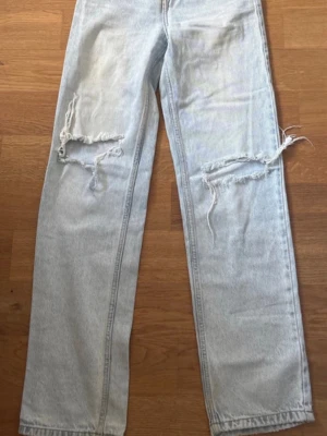 Ljusblå ripped jeans från FB Sister - Säljer ett par ljusblå raka jeans från FB Sister med stora slitningar över båda knäna. Jeansen har klassisk femficksmodell och är tillverkade i bomull. Perfekta för en avslappnad och trendig look.