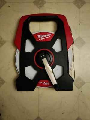 Milwaukee mätband 100m/330ft - Säljer ett långt mätband från Milwaukee på 100 meter (330 fot). Bandet har ett robust handtag i svart och rött plastmaterial samt en vev för enkel upprullning. Perfekt för större mätprojekt där precision krävs.