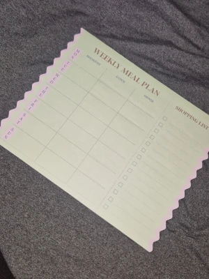 Veckoplanerare för måltider - Säljer en söt veckoplanerare för måltider i ljusgrönt papper med rosa vågig kant. Planeraren har kolumner för frukost, lunch och middag samt en inköpslista på sidan. Perfekt för att hålla koll på veckans mat och handling.