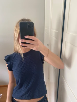 Mörkblå topp med volangärmar - Säljer en mörkblå topp. Köpt på Lindex på barnavdelningen men passar även XS. 