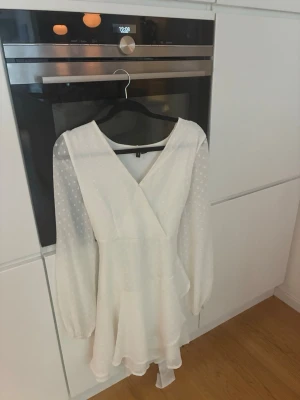 Vit omlottklänning med prickigt mönster - Supersöt vit klänning perfekt till studenten eller skolavslutningen. Klänningen är i bra skick och har bara använts ett fåtal gånger 💗
