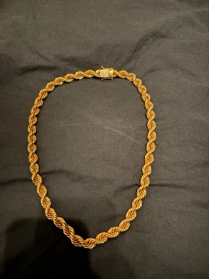 Tjockt guldfärgat tvinnat halsband - Snyggt halsband i guldfärg med tvinnad kedja som ger en exklusiv känsla. Halsbandet har ett dekorativt lås och känns rejält och trendigt. Perfekt accessoar för dig som vill sticka ut med en unik och iögonfallande stil. 10mm pris går att diskutera 