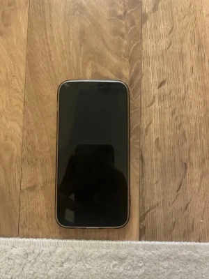 Mörkblå iPhone 12  mini med dubbla kameror - Säljer en svart iPhone 11 med stilren design och rundade kanter. Telefonen har en baksida i glas, två kameror och Apples logga i mitten. Perfekt för dig som vill ha en snygg och modern smartphone med bra prestanda och grym kamera.