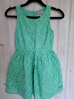 Mintgrön spetsklänning stl 140 - Superfin mintgrön kort klänning från Kappahl i spets med blommigt mönster. Ärmlös modell med rund halsringning och knappar i ryggen. Perfekt för sommarens alla tillfällen!