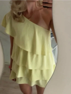 Gul one shoulder volangklänning - Söt gul kortklänning med one shoulder-design och flera volanglager. Storlek L men passar mindre!! Kontakta gärna innan köp