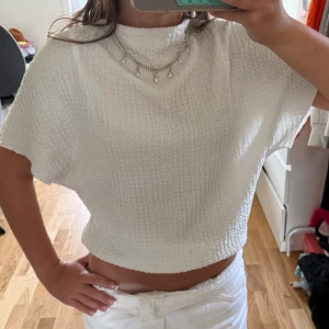 Vit topp i strukturerat tyg - Säljer en vit topp med boxig passform och korta ärmar. Toppen är gjord i ett strukturerat, lite tjockare tyg som ger en snygg textur. Perfekt till höga jeans eller kjol för en clean look.