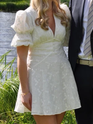 Adoore klänning - Vit miniklänning från Adoore med puffärmar och fina broderade blommor. Perfekt för sommarens alla tillfällen!! Endast använd 1 gång så den är i nyskick 💕
