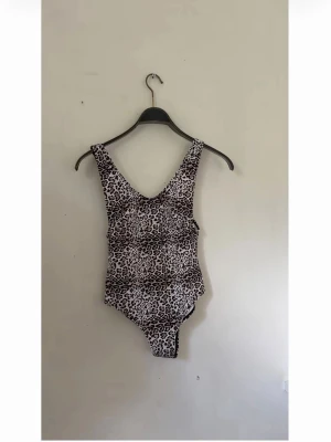 Leopardmönstrad baddräkt - Snygg baddräkt med leopardmönster i svart och vitt. Djup urringning både fram och bak, breda axelband och klassisk baddräktsmodell. Perfekt för dig som vill sticka ut på stranden eller vid poolen. Troligtvis i stretchigt syntetmaterial.