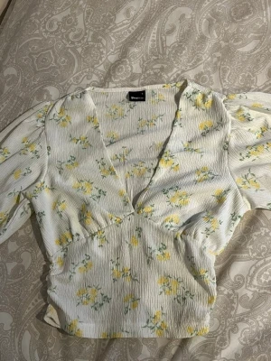 Blommig somrig blus🌿🌼 - Supersöt och somrig blus från Gina tricot!🌞🌼 vit med gula blommor och gröna blad.🍀 Blusen har v-ringning, puffiga långärmar och fungerar som en crop top! Supersnygg för dig som gillar somriga kläder! Fungerar jätte bra för fester, vardagar🫶🏼 Använt bara 1 gång till skolavslutningen!🤍Säljer mycket billigare än original pris!