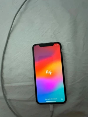 Vit iPhone 11 med dubbla kameror - Säljer en vit iPhone 11 med stilren glasbaksida och rundade kanter. Telefonen har två kameror på baksidan och den klassiska Apple-loggan. Skärmen är stor och har en tydlig notch upptill. Perfekt för dig som gillar snygg design och smarta funktioner.