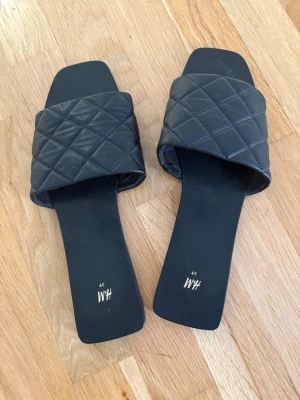 Svarta quiltade sandaler från H&M - Stilrena svarta sandaler från H&M med bred quiltad rem i konstläder och fyrkantig tå. Snygg minimalistisk design som passar perfekt till jeans eller kjol. Lätta att bara slinka i och dra ut på stan med. Klassisk look med modern twist.