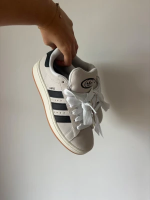 Adidas Campus 00s vita och svarta sneakers - Adidas Campus 00s. Storlek 39 1/3  Skick: helt oanvända med prislapp kvar.  Säljer då de inte kommit till användning. Klassiska och trendiga sneakers som passar till allt.  📦 Skickas samma dag vid köp innan kl 20  #vinted #adidas #adidascampus00s #campus00s #adidassneakers #sneakers #streetstyle #casualstyle #y2kfashion #unused #newwithtags