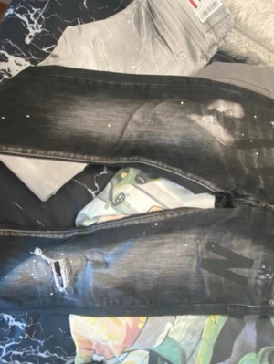 Svarta Dsquared2 jeans med slitningar - Säljer ett par svarta jeans från Dsquared2 med coola slitningar, färgstänk och en rå streetkänsla. 