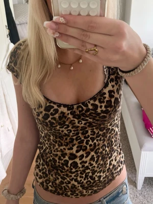Leopardmönstrad topp med kort ärm - Snygg leopardmönstrad topp med korta ärmar och rundad urringning. Toppens material känns mjukt och stretchigt, perfekt för dig som vill ha en figurnära passform. Matcha med jeans eller kjol för en trendig look.