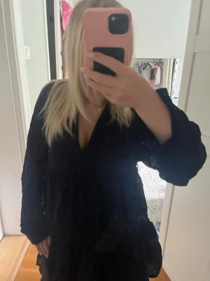 Mörkblå omlottklänning med volang - Säljer en mörkblå omlottklänning med v-ringning och volangdetaljer. Klänningen har lång ärm och en luftig passform som ger en skön och trendig look. Perfekt för dig som gillar stilrena och klassiska plagg.