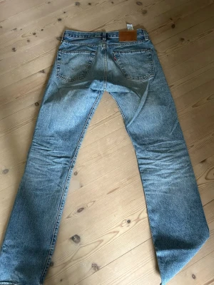 Levi's ljusblå raka jeans - Klassiska ljusblå jeans från Levi's med rak passform och fem fickor. Jeansen har en vintagekänsla med tydliga slitningar och den ikoniska läderlappen bak i midjan. Tillverkade i slitstark denim, perfekta för en avslappnad och tidlös stil.