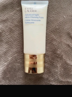 Estée Lauder micro cleansing foam  - Estée Lauder Advanced Night Micro Cleansing Foam i en elegant vit tub med guldfärgat lock. Rengöringsskummet är krämigt och passar perfekt för kvällsrutinen. Tuben har blå och guld text och känns lyxig och stilren.