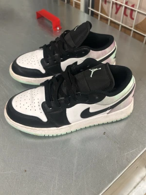 Air Jordan 1 Low svart/vit - Snygga Air Jordan 1 Low sneakers i svart och vitt med klassisk Jumpman-logga på plösen. Skorna har svart swoosh, svarta snören och vit sula med mintgröna detaljer. Ovandelen är i läder och mesh för både stil och komfort.