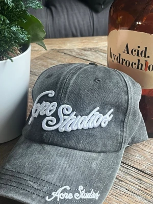 Grå keps från Acne Studios - Skriv innan köp         !!Säljer en grå keps från Acne Studios med broderad vit logga framtill och på skärmen. Kepsen har en klassisk böjd skärm och justerbar rem bak. Tillverkad i bomull med tvättad vintage-look som ger en avslappnad vibe.