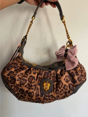 Juicy Couture handväska med rosett limited edition  - Cool handväska från Juicy Couture i leopardmönstrad sammet med mörkbruna läderdetaljer och guldfärgade kedjor. Väskan har en stor rosa rosett i sammet och ett emblem framtill. Perfekt accessoar för dig som gillar statement-plagg.