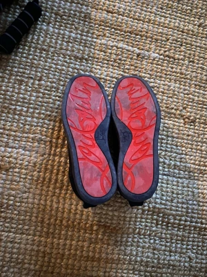  Christian Louboutin (loubs) - Snygga svarta sneakers från Christian Louboutin i mocka med klassiska röda sulor och logga undertill. Skorna har lågt skaft, svarta skosnören och en stilren design som sticker ut med den ikoniska röda undersidan. Storlek 40 men skulle säga att de passar 39 också! Använd 5-6 gånger kanske, ingen box eller något finns. OBS (vid köp skriv innan till mig!)