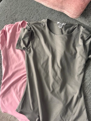 Två basic t-shirts i grått och rosa - Säljer två enkla t-shirts i mjukt bomullsmaterial, en i ljusgrå och en i ljusrosa. Båda har rund halsringning och korta ärmar, perfekta att matcha till jeans eller shorts. Stilrena och bekväma för en avslappnad look.