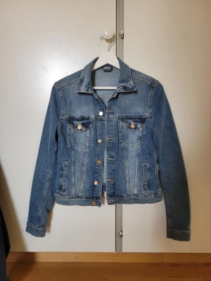 Blå jeansjacka - Säljer en klassisk blå jeansjacka med silverfärgade knappar.