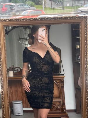 Svart kort spetsklänning - Säljer en svart kort klänning med v-ringning och spetsdetaljer.Klänningen har korta ärmar och figurnära passform med blommigt mönster i speten. Perfekt för dig som vill ha en elegant och trendig look. Klänningen kommer från shein, storlek 38. 