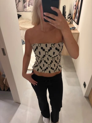 Vit och svart mönstrad tubtopp - Trendig vit tubtopp med svart abstrakt mönster. Toppen är axelbandslös och har en smockad, stretchig passform med vågig kant🌸