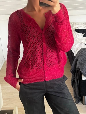 Hot pink virkad kofta med knappar - Snygg rosa kofta med virkat mönster och knäppning framtill. Långärmad modell med ribbade muddar vid ärmslut och nederkant. Perfekt för lager på lager och ger en trendig touch till din outfit.