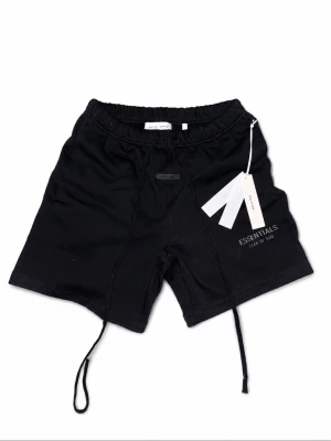 Svarta shorts från Fear of God Essentials - Svarta shorts från Fear of God Essentials med elastisk midja och långa snören framtill. Diskret logga på vänster ben och mjukt material som känns skönt mot huden. Perfekta för en avslappnad och trendig look.