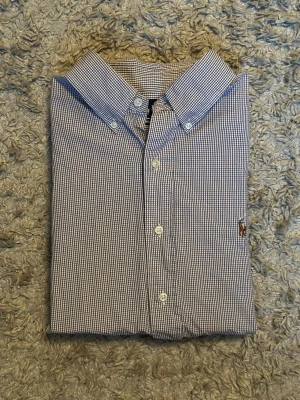 Rutig skjorta från Ralph Lauren - Klassisk långärmad skjorta från Ralph Lauren i blåvitt småmönstrat rutigt tyg. Skjortan har button-down krage, vita knappar och den ikoniska broderade loggan på bröstet. Tillverkad i bomull för en skön och luftig känsla.