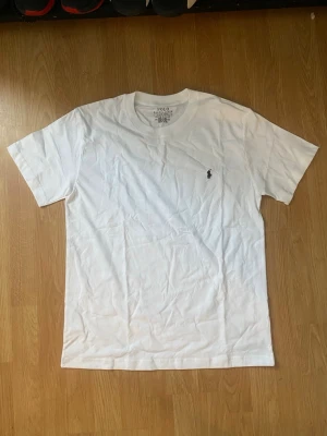 Ralph Lauren T-Shirt - Vit t-shirt från Polo Ralph Lauren med klassisk passform och korta ärmar. Diskret logga broderad på bröstet. Gjord i mjuk bomull som känns skön mot huden. Perfekt för dig som gillar stilrena basics.
