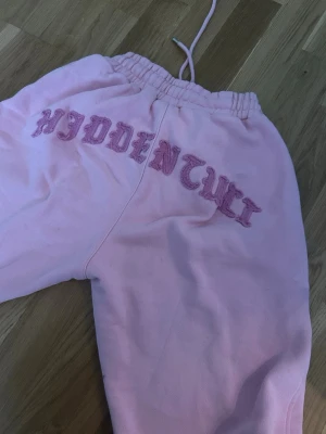Rosa mjukisbyxor från hidden cult är xss men passar som xs  - Säljer ett par ljusrosa mjukisbyxor från Hiddentull med broderad logga i rosa på framsidan. Byxorna har resår i midjan och dragsko för skön passform. Tillverkade i mjukt bomullsmaterial, perfekta för chill dagar eller streetwear-stil.