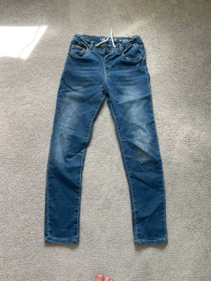 Blå slim fit jeans från LAB industris - Säljer ett par blå slim fit jeans från lab industri med klassisk femficksdesign och snygga slitningar på framsidan. Jeansen har normal midja, bälteshällor och är för extra komfort.