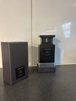 Tom Ford Oud Wood Eau de Parfum 100ml - Tom Ford Oud Wood Eau de Parfum i 100 ml flaska. Flaskan är mörkgrå och elegant med en fyrkantig form och svart etikett. Kommer med originalkartong i matchande färg. En exklusiv doft med lyxig känsla och stilren design. 