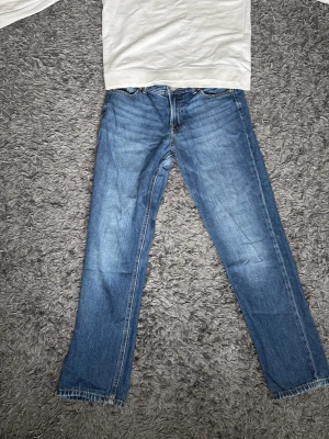 Blå raka jeans i klassisk modell och Prada tröja med röda detaljer  - Säljer ett par blå jeans med rak passform och klassisk femficksdesign. Jeansen har en snygg tvättad look och är tillverkade i denim. Perfekta för en avslappnad och stilren outfit.