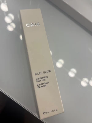 CAIA Bare Glow skin tint - Säljer en CAIA Bare Glow perfecting skin tint i nyansen 30. Kommer i en stilren beige förpackning med silverdetaljer och rymmer 30 ml. Perfekt för dig som vill ha en naturlig glow och lätt täckning. Enkel att applicera och ger en fräsch finish.