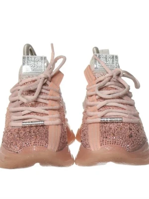 Glittriga sneakers från SMR - Snygga sneakers från SMR i persikofärg med massor av glittrande stenar över hela ovandelen. Skorna har tjock, transparent sula och breda, ljusrosa snören. Märkeslogga på plösen och cool design som sticker ut. Perfekta för dig som vill ha något extra till din outfit.