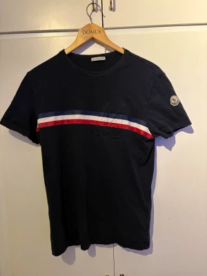 Marinblå Moncler t-shirt med ränder - Storlek M passar bäst till S alltså liten i storlek OBS lite konstig storlek för den är från 2016 alltså gammal model av moncler 